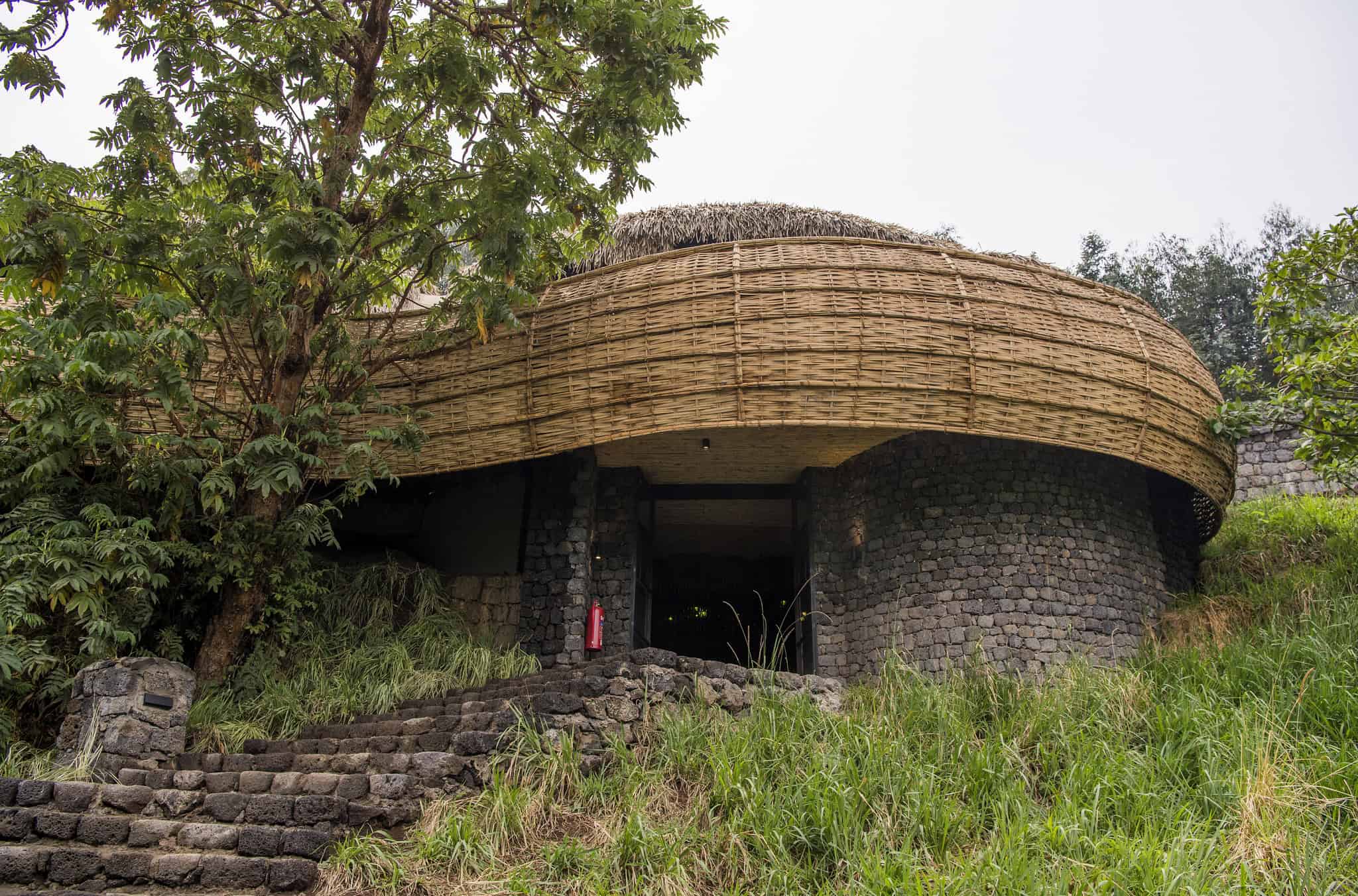 Eco-friendly lodge built on a hillside with natural stone and thatched roof, surrounded by lush greenery.