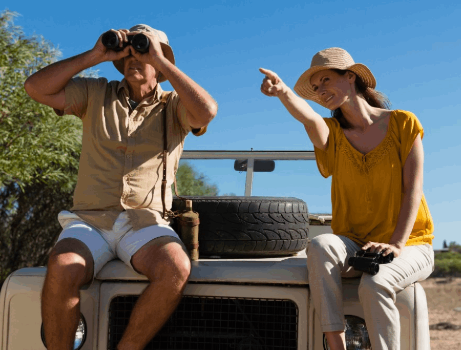 Two safari enthusiasts with binoculars and camera on a vehicle during a game drive.